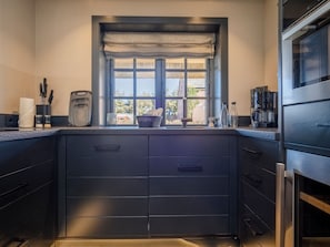 A modern kitchen with dark cabinetry, a window with a view of the outdoors, and a coffee maker on the counter.