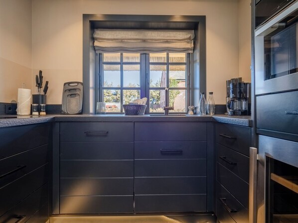 A modern kitchen with dark cabinetry, a window with a view of the outdoors, and a coffee maker on the counter.