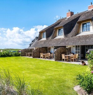 Un bâtiment traditionnel à toit de chaume, doté d’une terrasse et d’une pelouse bien entretenue.