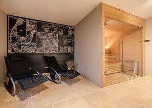 Ein moderner Wartebereich mit schwarzen Lounge-Stühlen, einer großen Karte an der Wand und einer Holztür zu einem Duschbereich.
