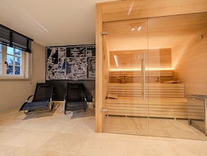 Una sala de sauna con bancos de madera y puerta de vidrio, una ventana con persianas y una pared con mapas.