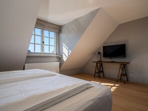 Une chambre à coucher avec un lit, un téléviseur posé sur un meuble en bois et une fenêtre donnant sur le ciel.