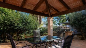Une terrasse extérieure avec une table et des chaises en verre, entourée de verdure.