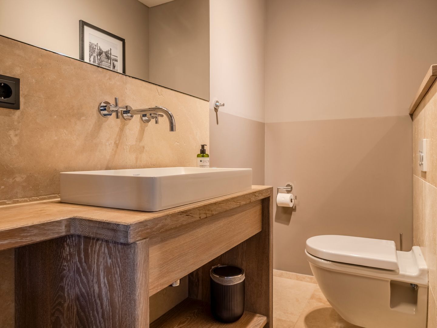 Een moderne badkamer met een houten wastafelmeubel, een witte wasbak en een toilet.
