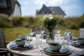 Ein runder Outdoor-Esstisch, gedeckt mit Tellern, Schüsseln und Weingläsern, mit einem Blumenstrauß in der Mitte.
