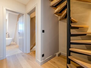 Ein modernes Interieur mit einer Treppe, einem Badezimmer mit freistehender Badewanne und einem Flur, der in einen weiteren Raum führt.
