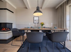 A modern dining area with a wooden table, black chairs, a fireplace, and a hanging light fixture.
