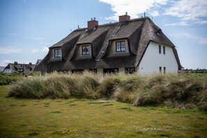 A traditional house with a thatched roof, a white exterior, and a visible chimney.
