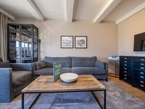 A modern living room with a grey sofa, a coffee table with a bowl, a cabinet with glass doors, and two framed pictures on the wall.