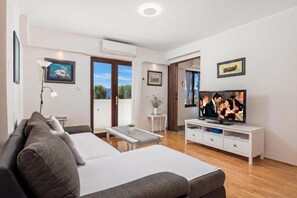 A modern living room with a sofa, a TV, and a balcony with a view.