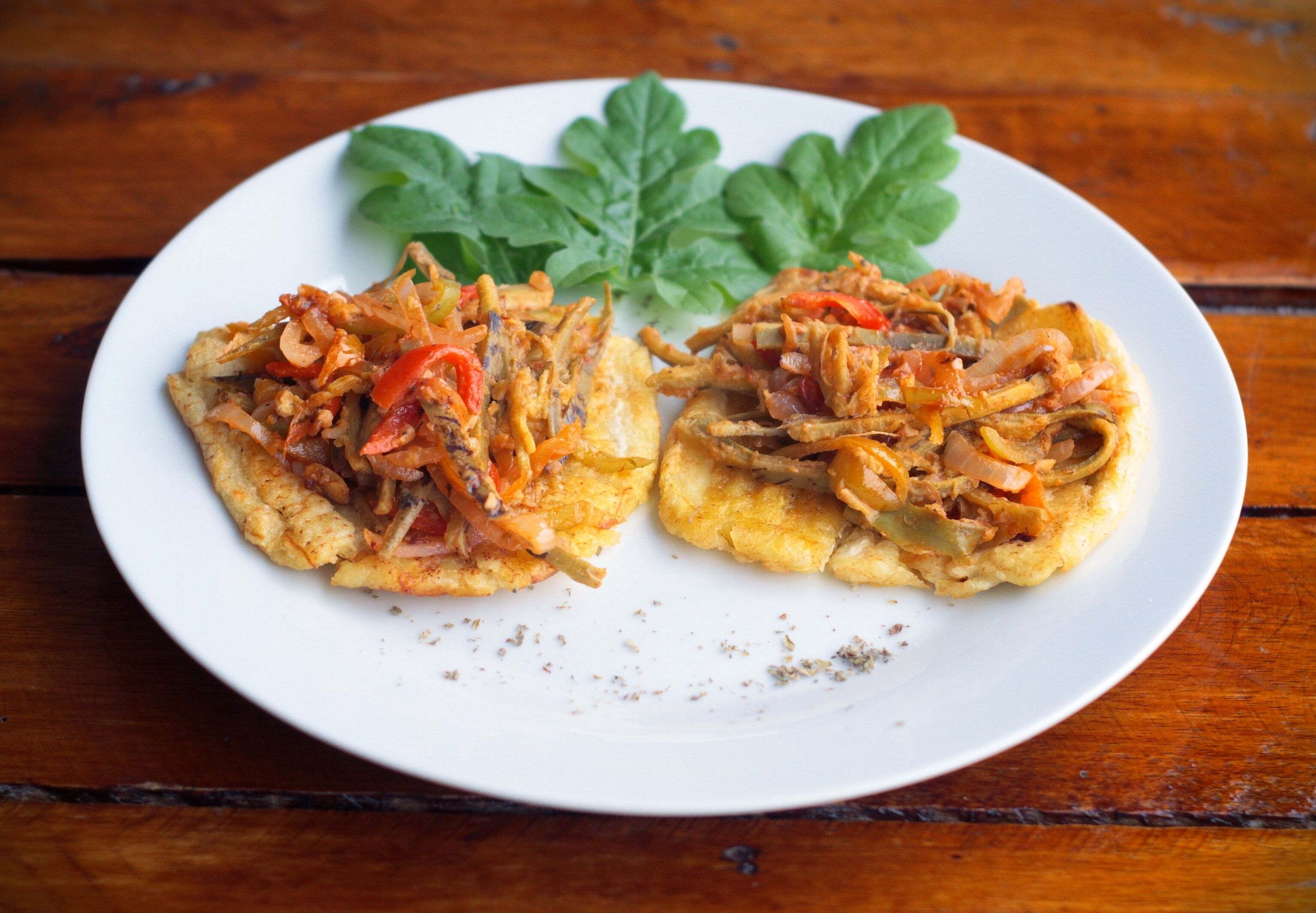 Une assiette contenant deux aliments frits, recouverts de légumes et décorée d’une feuille.