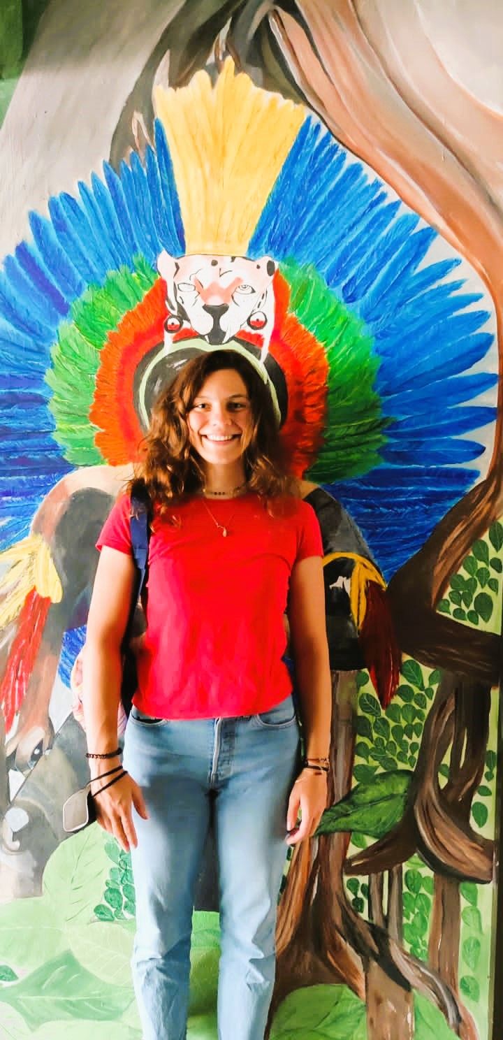 Une personne se tient devant une fresque colorée représentant un arbre et un lion.