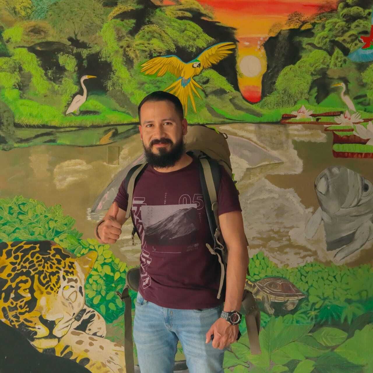 Un homme se tient devant une fresque murale représentant une scène de jungle, avec un perroquet, un léopard et une tortue.