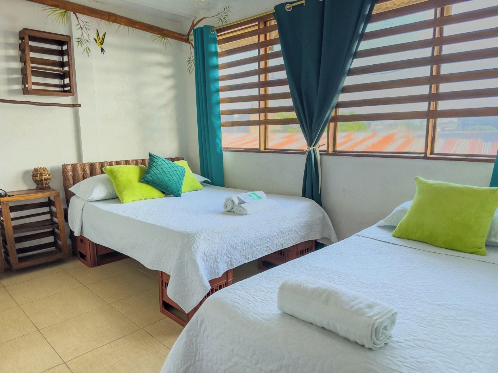 A hotel room with two beds, a wooden headboard, a small table, and a window with curtains.