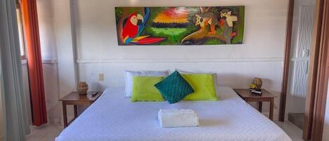 A bedroom with a large bed, a painting above it, and a wooden ceiling.
