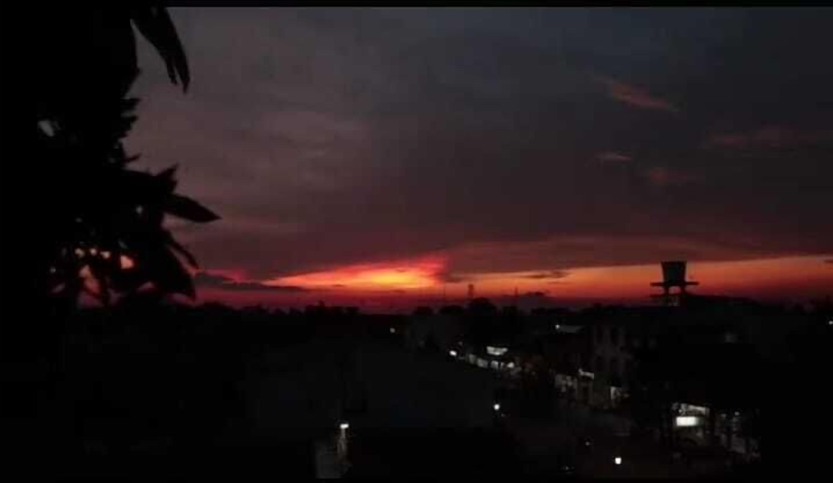 A sunset with a silhouette of a building and trees in the foreground.