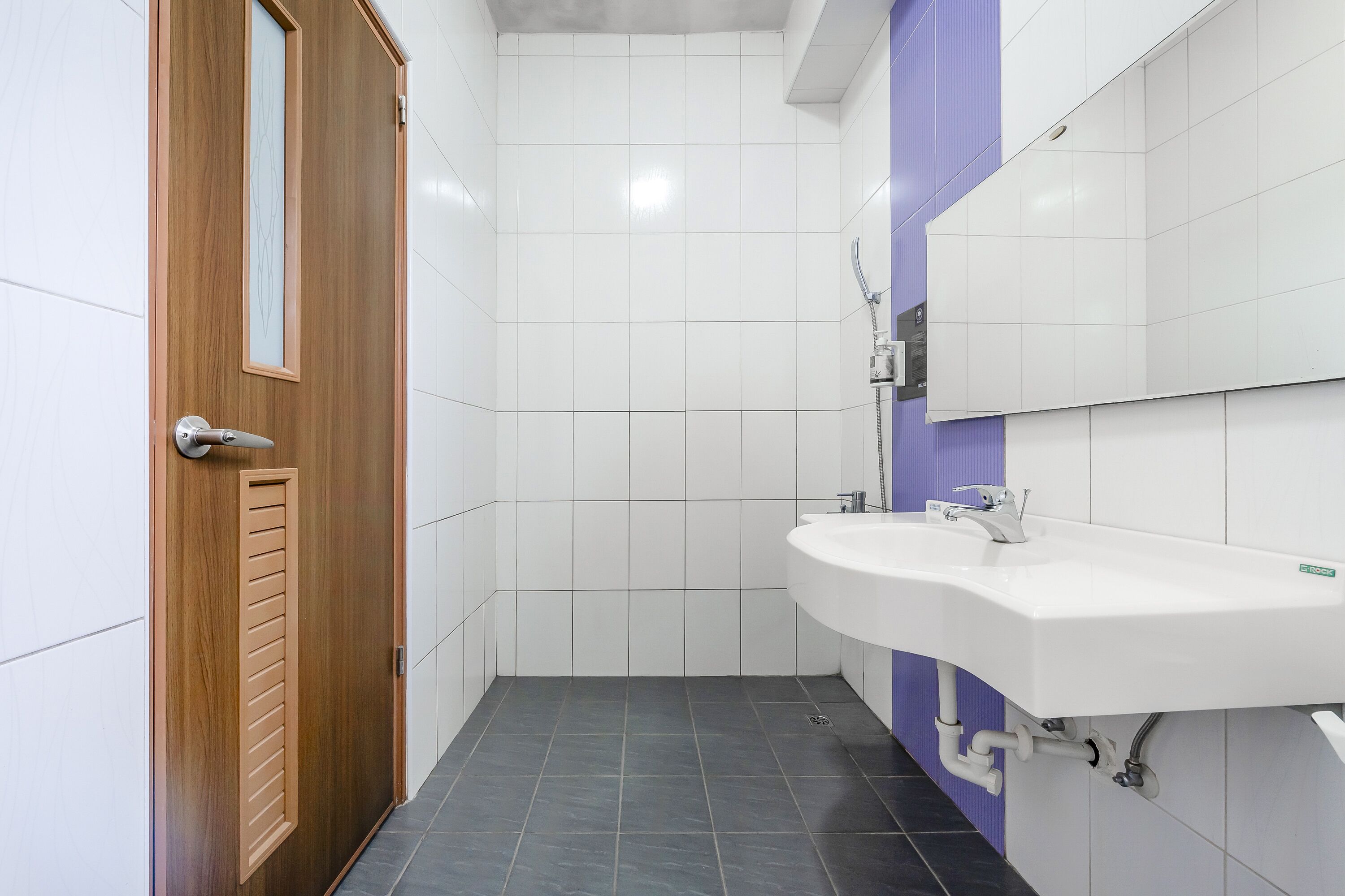 Un baño con puerta de madera, paredes de azulejos blancos, un lavabo blanco y zona de ducha.