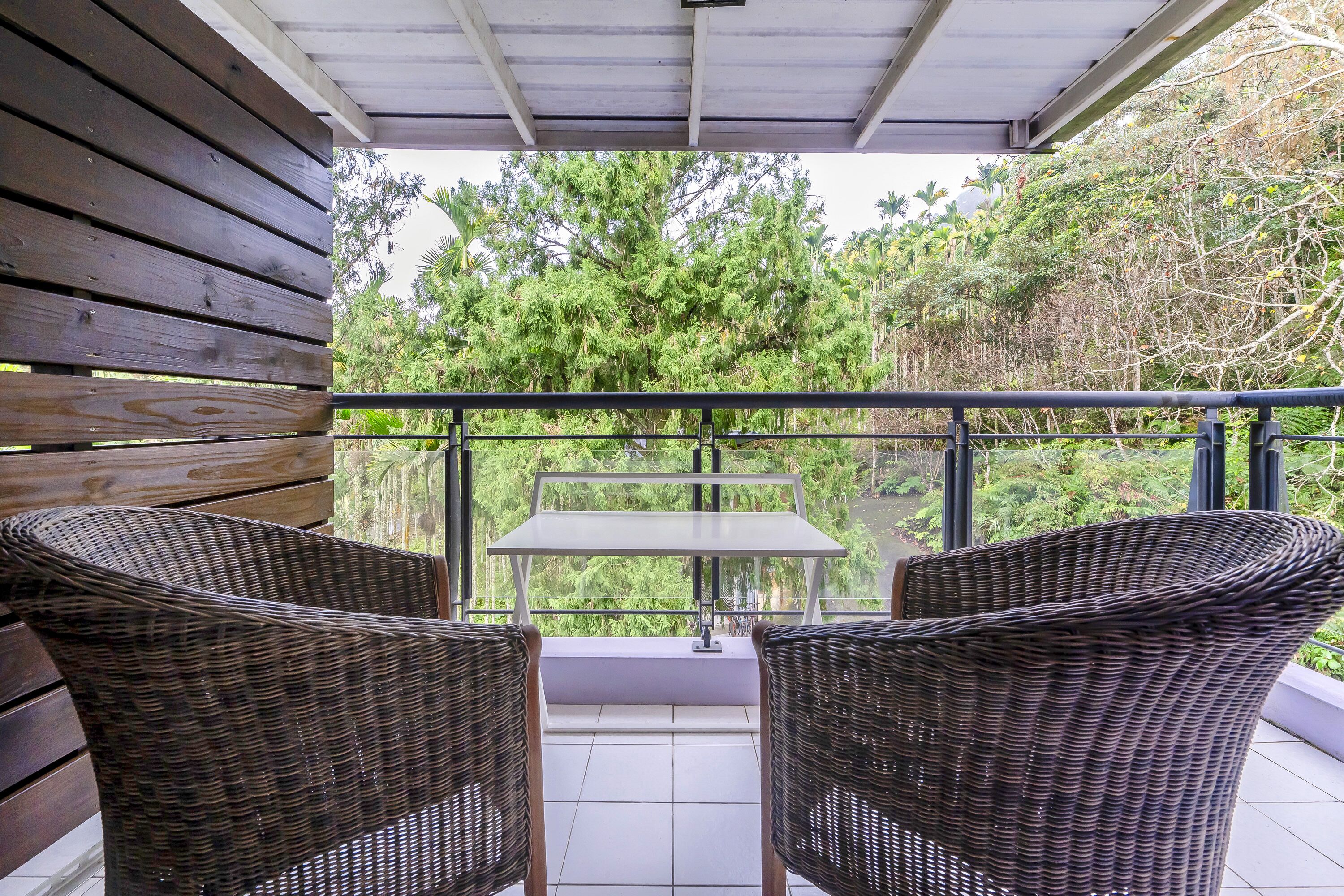Un balcón con sillas de mimbre y una mesa, con vistas a un jardín exuberante.