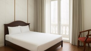 A neatly made bed with a wooden headboard, a wooden chair with a red cushion, and a view of a balcony through sheer curtains. - TUAN CENTRAL HOTEL (Hanoi)