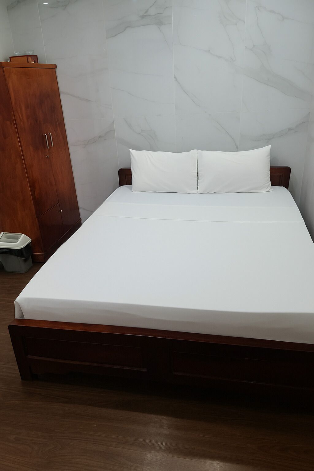 Ein ordentlich bezogenes Bett mit weißer Bettwäsche in einem Zimmer mit Marmorwänden und einem Holzschrank.