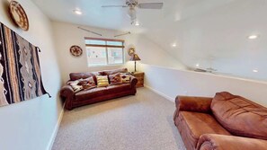 A spacious loft with a high ceiling, a brown leather sofa, a smaller brown sofa, a patterned rug, and a ceiling fan. - Rim Vistas - 4A4 (Moab)