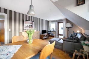 Ein modernes Wohnzimmer mit Essbereich, einer Couch, einem Fernseher und einer Treppe.