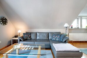 Ett modernt vardagsrum med en grå soffa, ett soffbord i glas, ett sidobord med en lampa och en klocka på väggen.