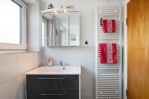 Ein Badezimmer mit einem weißen Waschbecken, dunklen Schränken, einem beleuchteten Spiegel und einem Handtuchhalter mit roten Handtüchern.