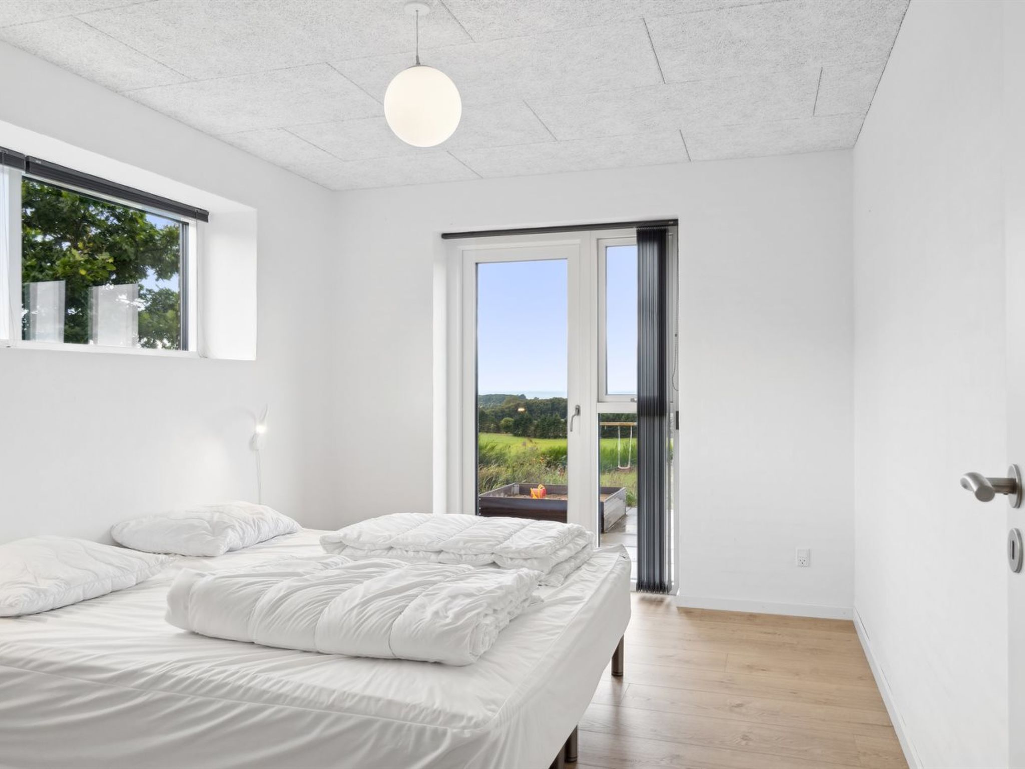 A modern bedroom with a large bed, a window, and a door leading to a balcony.