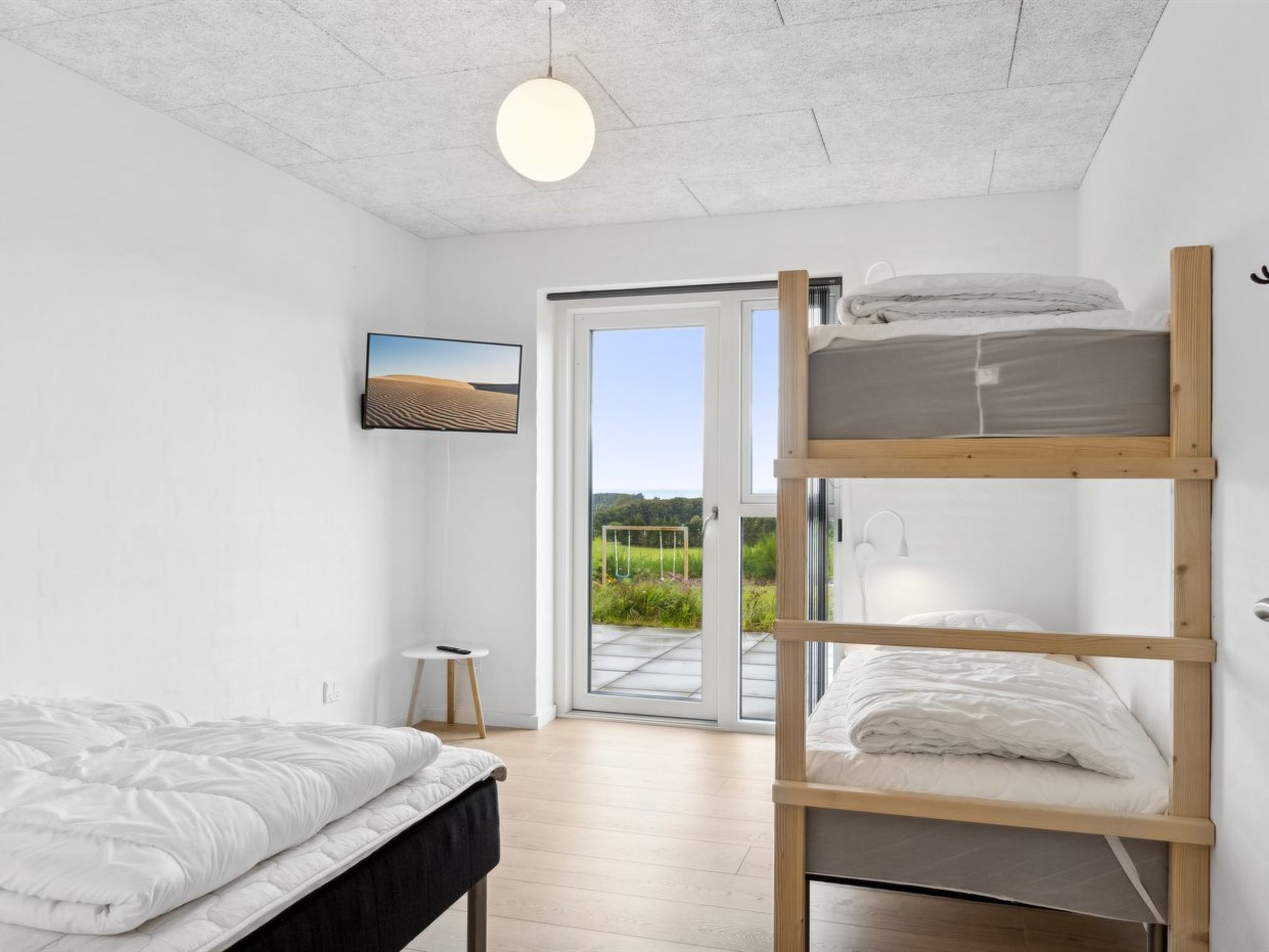 Quarto moderno com cama beliche, uma cama individual, televisão e vista para o exterior.