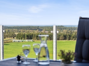 Een tafel met drie glazen en een vaas, met uitzicht op een groen landschap met hooibalen en bomen.