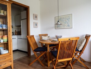 Uma sala de jantar com cadeiras de madeira e uma mesa, cozinha ao fundo e um mapa na parede.