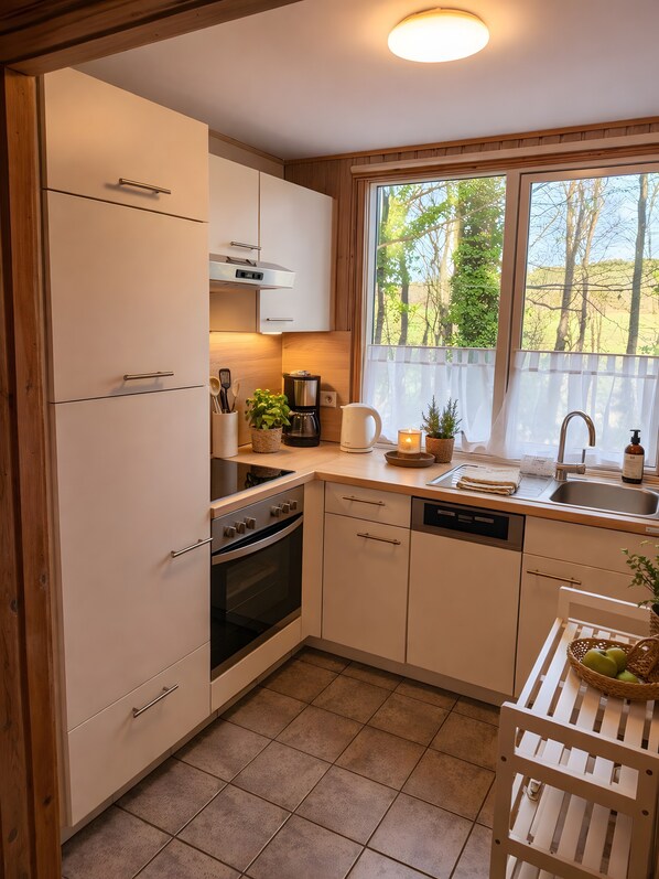 A modern kitchen with white cabinets, a built-in oven, a coffee maker, and a window with a view of trees.