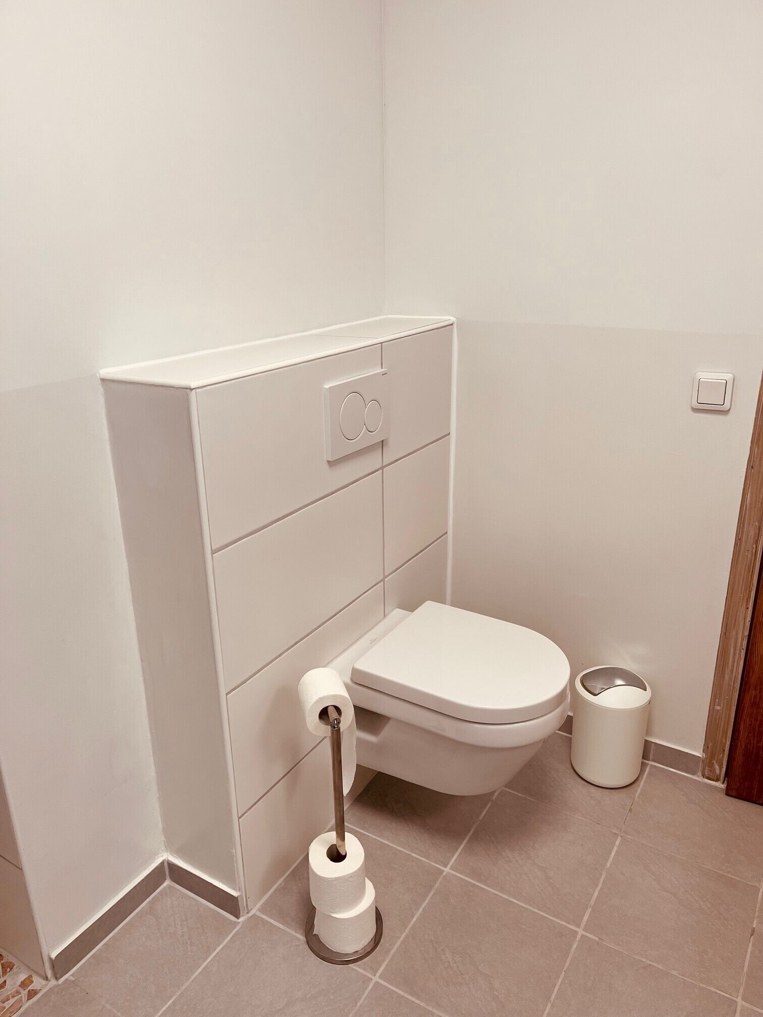 Ein kleines, sauberes Badezimmer mit Toilette, Papierhalter und Mülleimer.