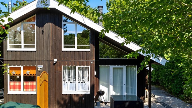 Ein modernes, zweistöckiges Haus mit geneigtem Dach, großen Fenstern und einer überdachten Terrasse.