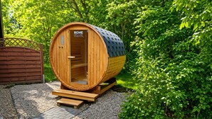 Eine Holzsauna mit einer Tür, auf der 'HOME DELUXE' steht, in einer Gartenanlage.
