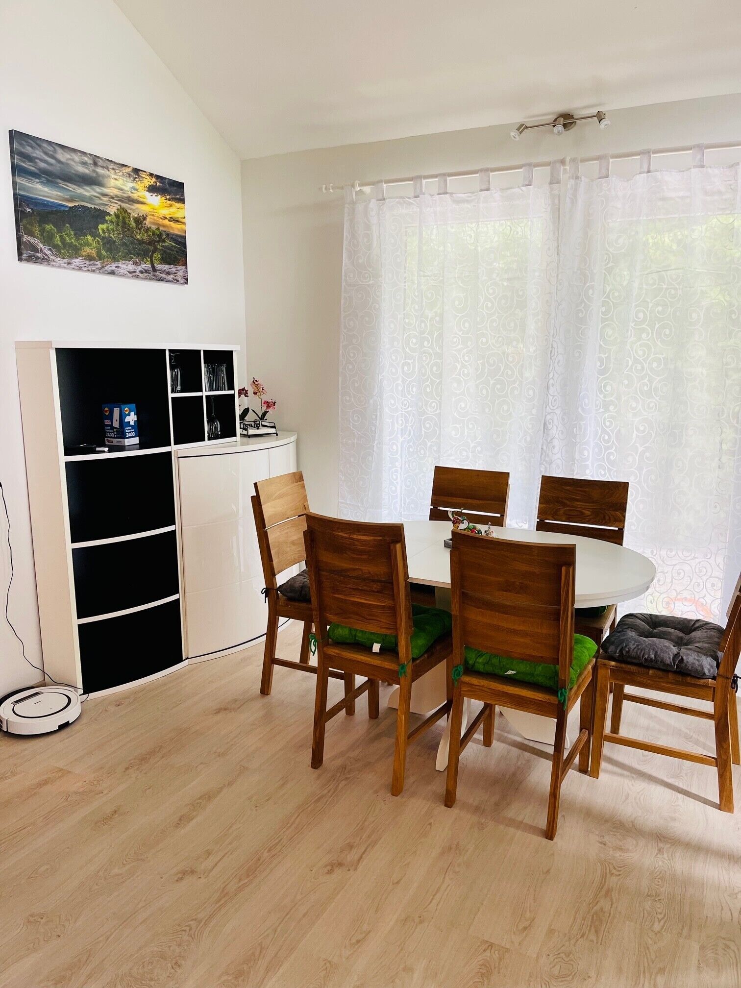 A dining area with a table and chairs, a cabinet with shelves, and a painting on the wall.