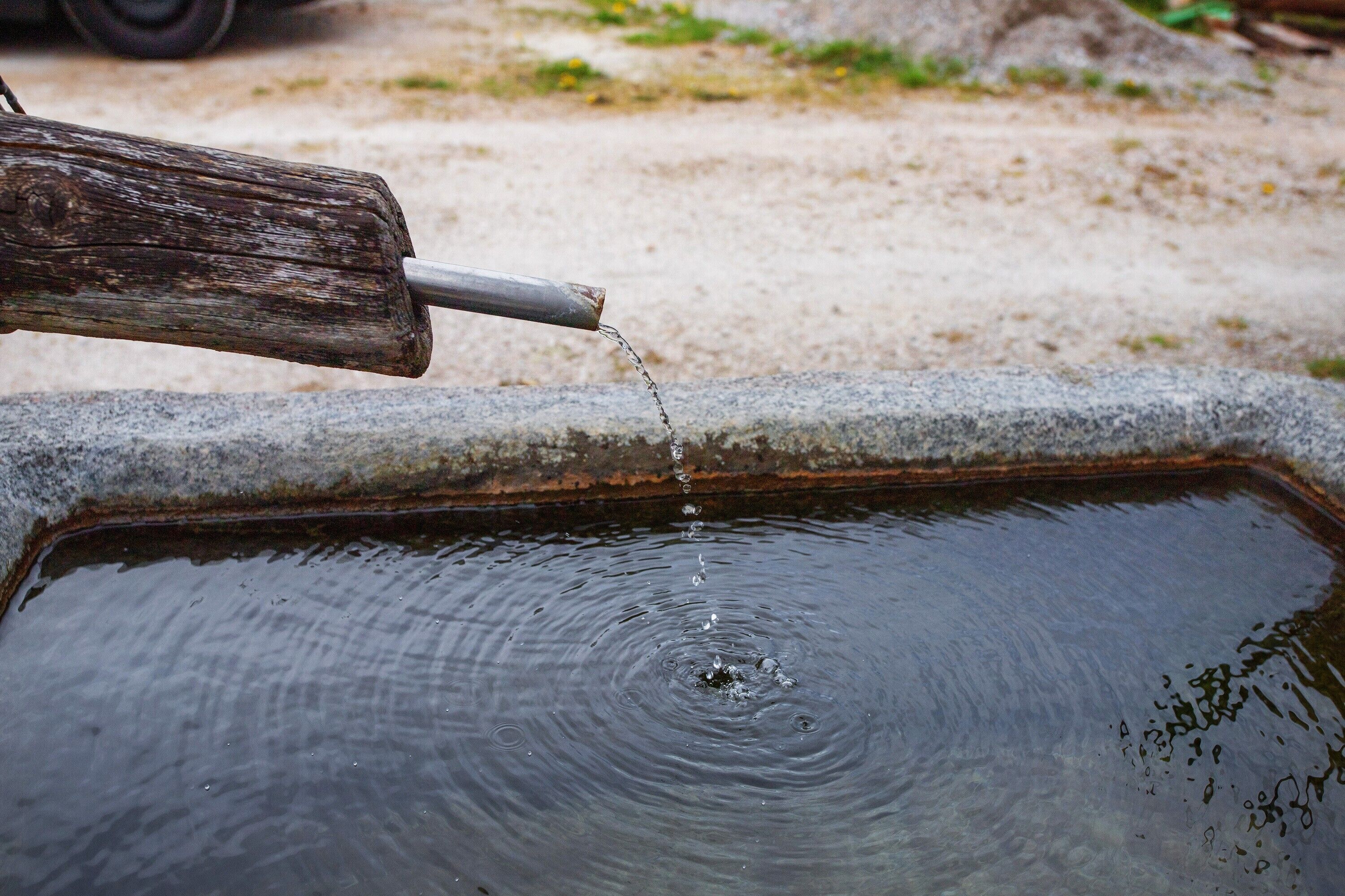 A metal spout pouring water into a rectangular basin.
