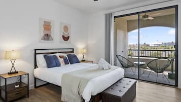 Una habitación de hotel moderna con una cama grande, dos mesitas de noche con lámparas, un banco y un balcón con sillas.