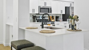 A modern kitchen with white cabinets, stainless steel appliances, and a central island with a sink and stools. - TWO Glendale CozySuites with Pool 2 & 9 (Glendale)