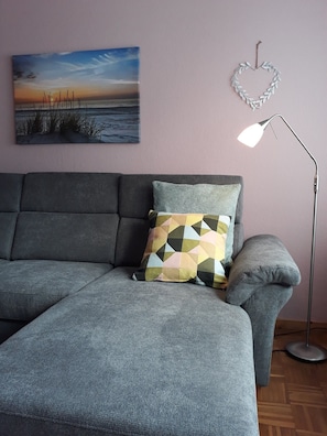 Un canapé gris orné d’un coussin à motifs géométriques, un tableau accroché au mur et une lampe sur pied.