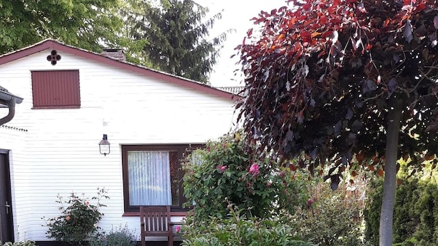 En hvid bygning med røde døre og vindueskasser, omgivet af en have med forskellige planter og blomster.