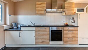 Una cuina moderna amb armaris blancs, forn d'acer inoxidable i microones.