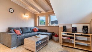 Un saló modern amb un sofà modular, una taula de centre, un moble de televisió amb altaveus i un rellotge a la paret.