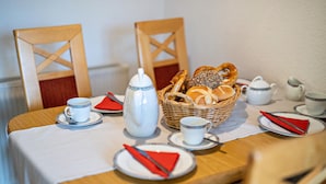 Una mesa de comedor dispuesta con platos, cubiertos, una tetera, tazas y una cesta de pan.