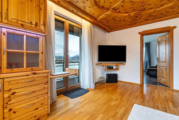 Un intérieur en bois avec une télévision, des meubles en bois et une vue sur l’extérieur grâce à une grande fenêtre.