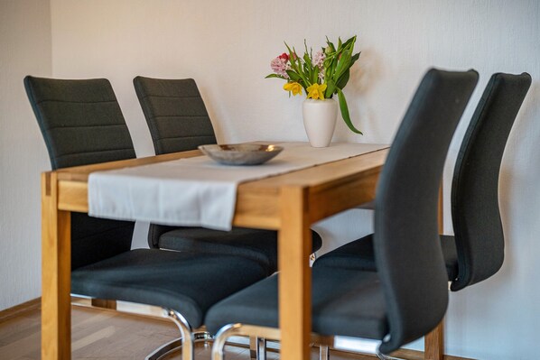 Una mesa de comedor con cuatro sillas, un jarrón blanco con flores y un tazón sobre la mesa.