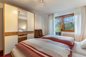 Camera da letto con un letto grande, un armadio, una finestra con tende e vista su alberi.