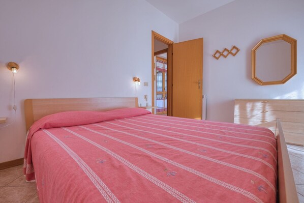 A bedroom with a wooden bed, a nightstand with a lamp, a wardrobe, and a mirror on the wall.
