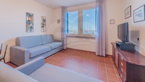 Una sala de estar con sofá, televisor y ventana con vista al mar.